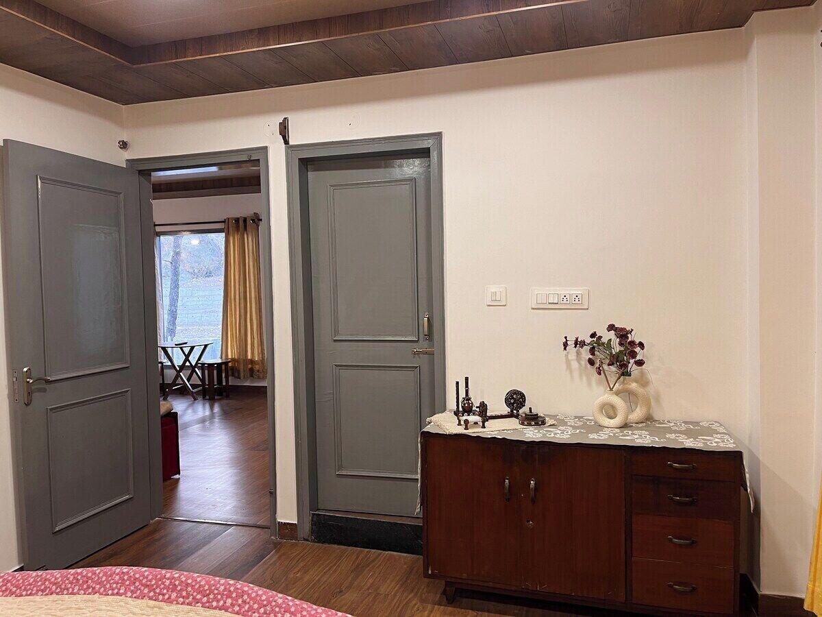 A room with a wooden dresser, a desk with a vase, and a door leading to another room.