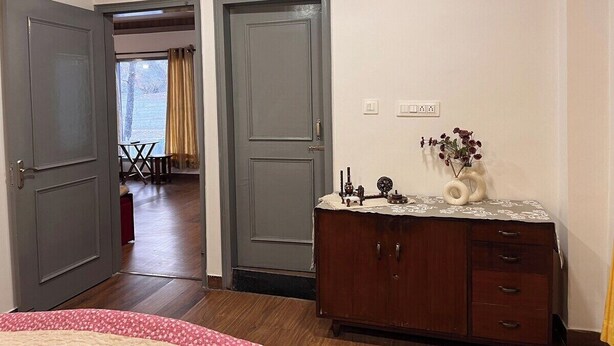 A room with a wooden dresser, a desk with a vase, and a door leading to another room. - Rustic Pines (Solan)