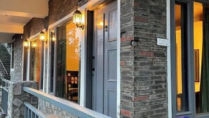 A building with a stone facade, a balcony with a metal railing, and a door with a light fixture above it. - Rustic Pines (Solan)