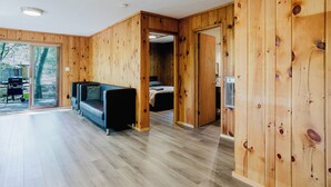A modern interior with wooden walls, a sofa, a bed, and a sliding glass door leading to an outdoor area. - 2 Bedroom Cottage XI: SB (Carling)