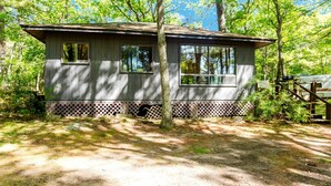 A small cabin with two windows, surrounded by trees and a wooden fence. - 2 Bedroom Cottage XI: SB (Carling)