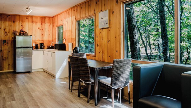 A modern kitchen with wooden walls, a dining area with a table and chairs, and a large window offering a view of trees. - 2 Bedroom Cottage XI: SB (Carling)