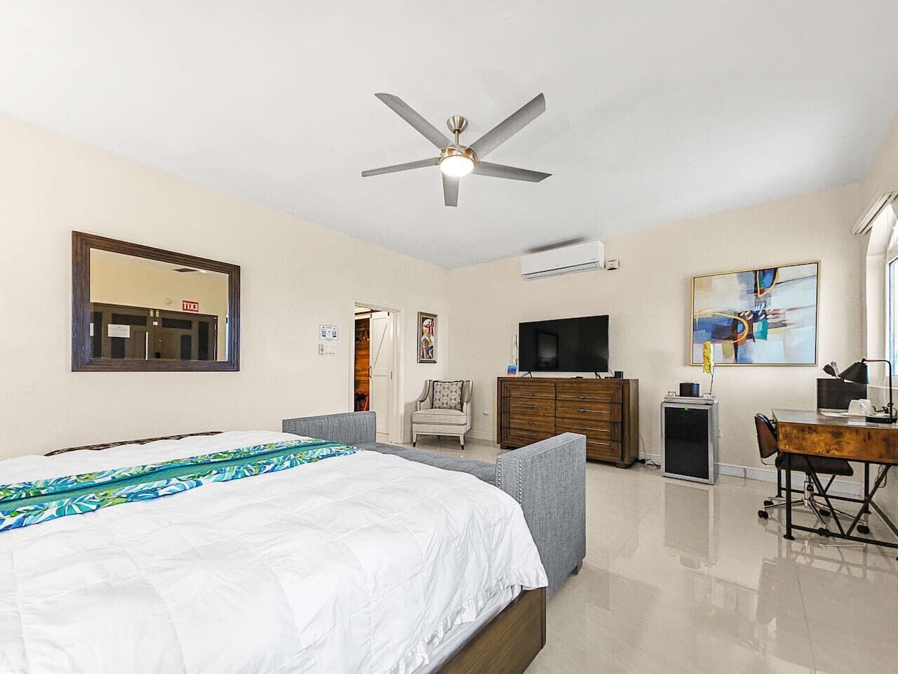 A bedroom with a bed, a desk, a chair, a television, and a ceiling fan.