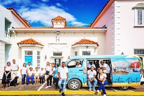 A group of people standing in front of a building with a sign that reads "HOSPITALITY EXPERT." - BTS7 (Montego Bay)
