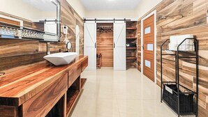 Un baño moderno con tocador de madera, un lavabo y un espejo. Se ve una zona de ducha al fondo.