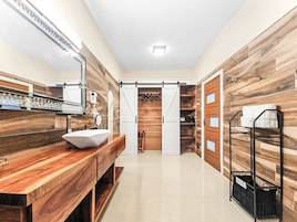 Un baño moderno con tocador de madera, un lavabo y un espejo. Se ve una zona de ducha al fondo.