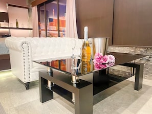 A modern living room with a white leather sofa, a glass coffee table with a bottle and flowers, and a cityscape view through the window. - hotel parkside (Tokyo)