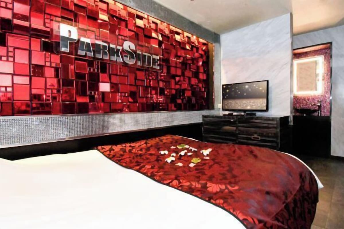A hotel room with a large bed, a TV, and a wall with the word 'PARKSIDE' on it.