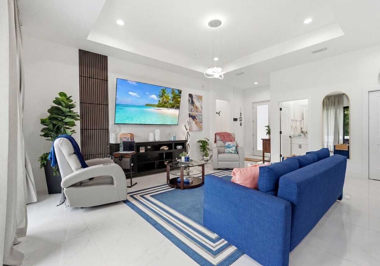 A modern living room with a large flat-screen TV, a blue sofa, a white recliner, and a coffee table.