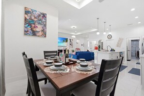 A modern dining area with a wooden table set for four, a kitchen in the background, and a living area with a blue sofa. -   Spacious 3-BD Home with Private Hot Tub Near the Beautiful Boca Grande Beaches (Placida)