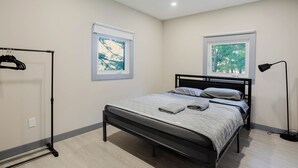 Une chambre à coucher avec un lit, deux fenêtres, un lampadaire noir et un portant à vêtements.