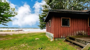 Une petite cabane en bois dotée d’une véranda, située dans une zone herbeuse, d’où l’on peut admirer une plage et la mer en arrière-plan.
