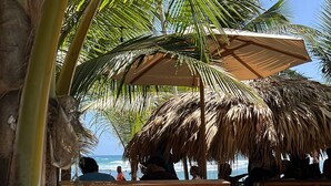 A beachside seating area with wooden benches and a thatched umbrella, overlooking the ocean. - Penthouse Overlooking  the Marina and Sea with 4-bedrooms and Pools (Fajardo)