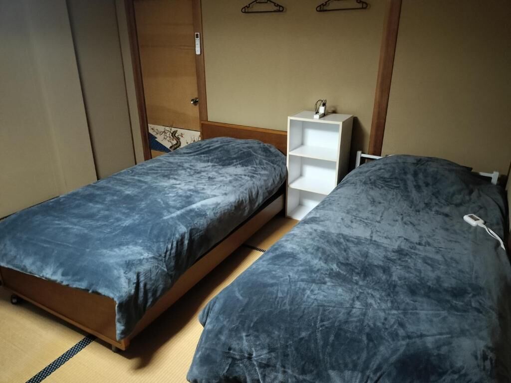 Quarto com duas camas, uma estante branca e um guarda-roupa de madeira.