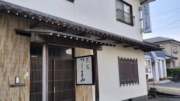 Un bâtiment traditionnel japonais, doté d’une entrée en bois, d’un porche carrelé et d’une enseigne avec des caractères japonais.