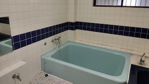 A bathroom with a rectangular bathtub, white tiled walls, and a blue-tiled accent strip. - Guesthouse Naruto Ohenro (Naruto)