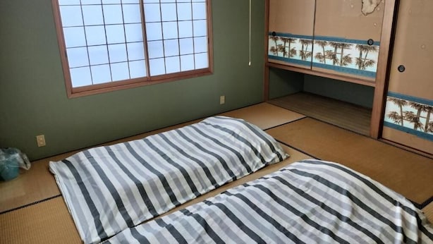 A room with tatami flooring, a futon bed, a shoji screen, and a traditional Japanese-style wardrobe. - Guesthouse Naruto Ohenro (Naruto)