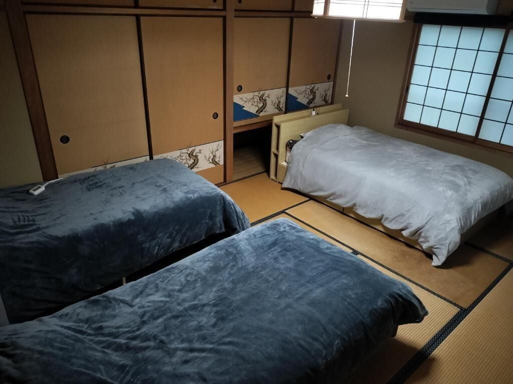Et traditionelt japansk værelse med tatamimåtter, to enkeltsenge med blåt sengetøj, et indbygget skrivebord og skydedøre.