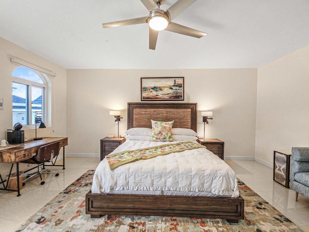 A bedroom with a bed, desk, chair, and a ceiling fan.