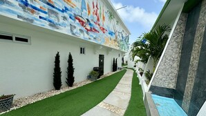 Pasillo de hotel con césped artificial, un camino de piedra, un mural en la pared y una zona de piscina.