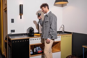 Une petite cuisine équipée d’une machine à café, d’un évier et d’une étagère avec des en-cas.