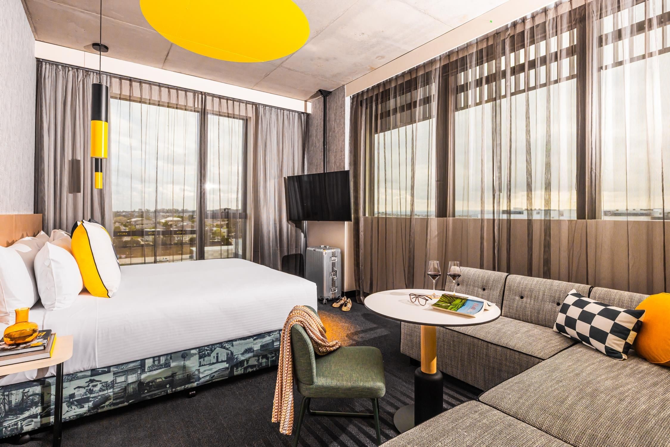 A hotel room with a bed, a sofa, a small table, a TV, and a view of the city.