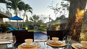 A dining area with a view of a swimming pool, outdoor seating, and a stone wall. - Luxury Private 3BR Villa with Private Pool Near Pereybere Beach  Sleeps 6 (Grand Baie)