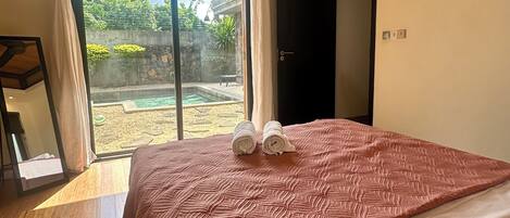 A bedroom with a large bed, a ceiling fan, a sliding glass door to a courtyard, and a dark door.