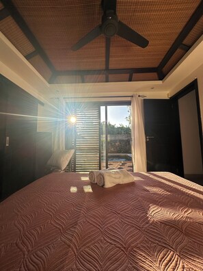 Ein Schlafzimmer mit einem Bett, einem Deckenventilator, Blick durch ein Fenster und einer Tür.