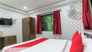 Habitación de hotel con cama, televisor montado en la pared, armario y ventana con cortinas.