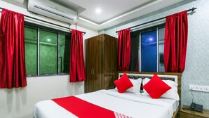 Una habitación de hotel con cama, cortinas rojas, un armario y un teléfono en la mesita de noche.