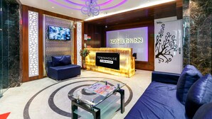 Zona de recepción de un hotel con diseño moderno, que incluye un mostrador de recepción, un área de descanso y una pantalla de televisión.