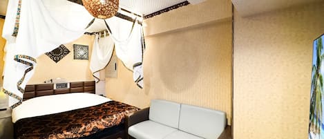 A bedroom with a bed, a white sofa, a glass coffee table, and a decorative hanging light fixture.