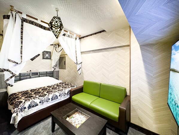 A bedroom with a bed, a green sofa, a nightstand, and a decorative hanging light fixture.