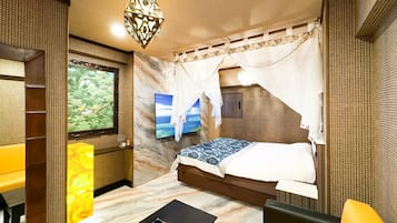Habitación de hotel con cama, televisión, una pared decorativa y una mesita con un arreglo floral.