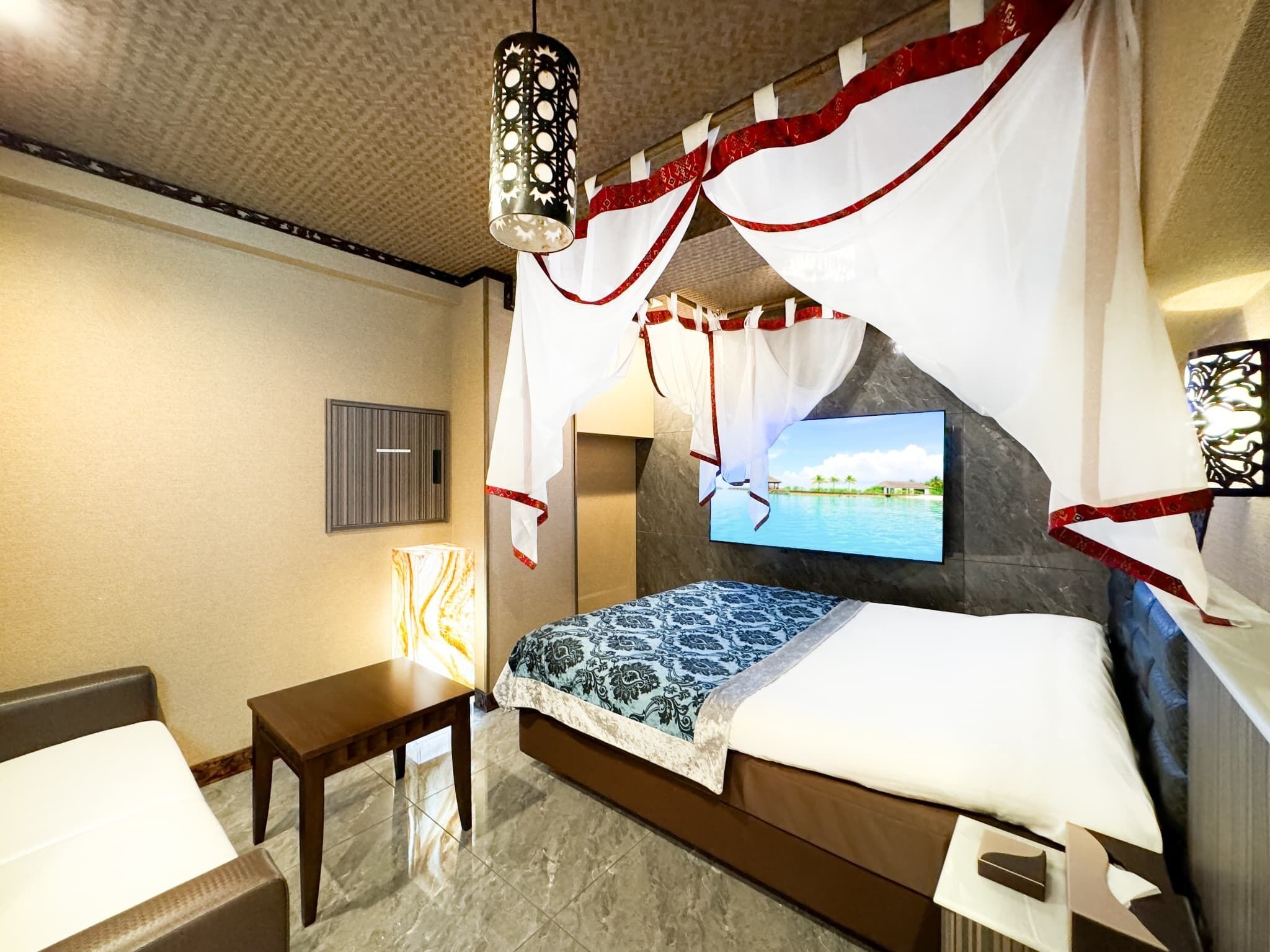 A hotel room with a bed, a TV mounted on the wall, a bedside table, and a lamp.