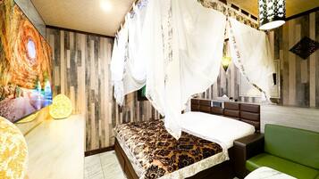 Un dormitorio con una cama, un sofá verde, un televisor montado en la pared y una lámpara decorativa.