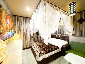 Un dormitorio con una cama, un sofá verde, un televisor montado en la pared y una lámpara decorativa.