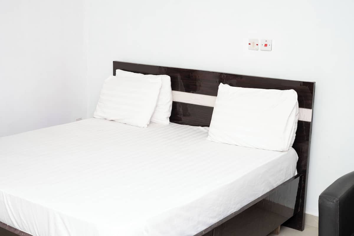 Una cama con ropa blanca, cabecera de madera oscura y dos interruptores de luz en la pared.