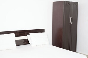 Un lit avec une literie blanche et deux oreillers, une armoire en bois foncé à deux portes et un mur blanc uni.