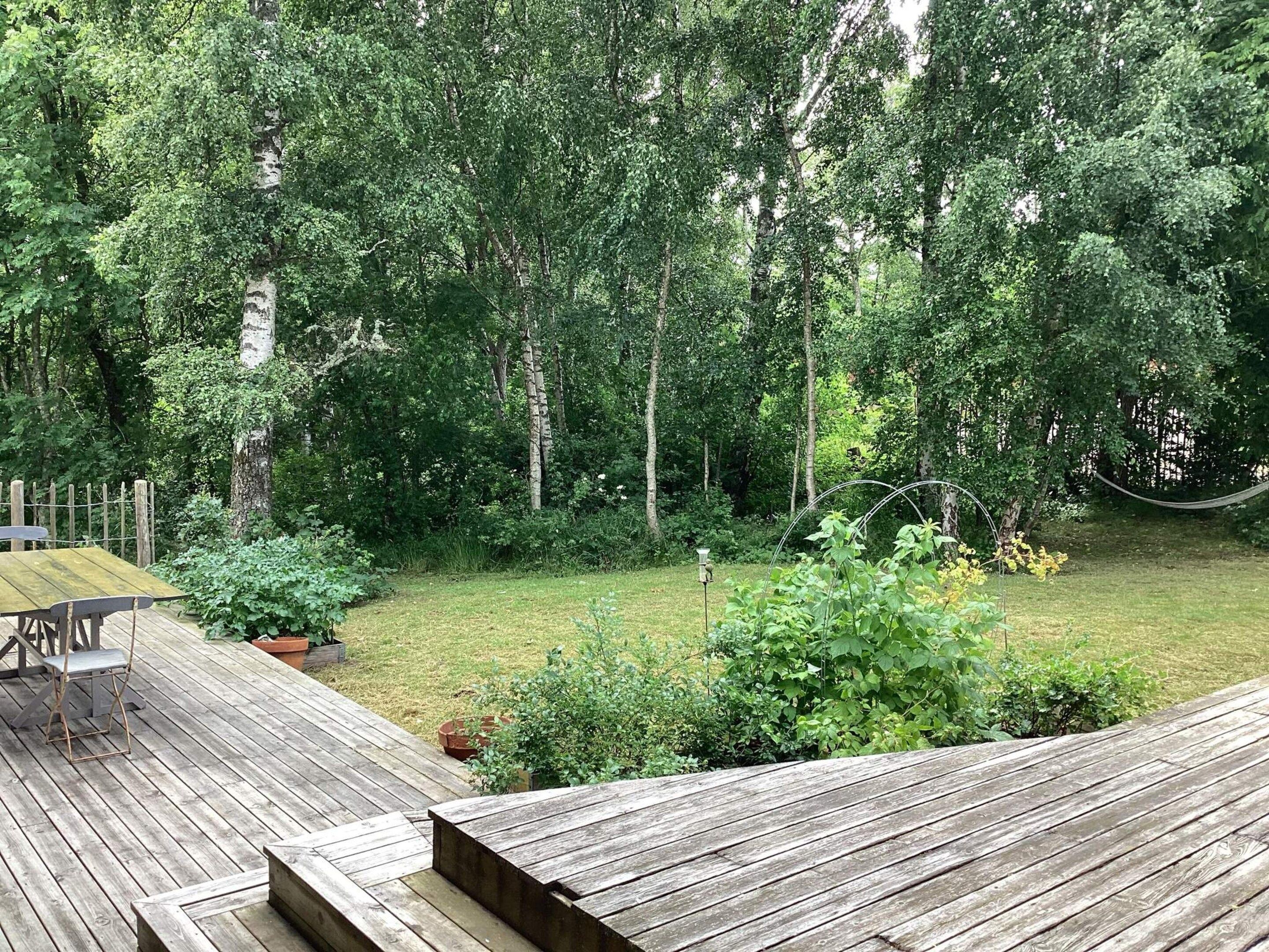Un terrazzo in legno con tavolo e sedie, immerso in un rigoglioso giardino ricco di piante e alberi.