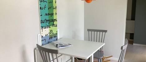 A dining area with a white table, grey chairs, a colorful wall with handwritten notes, and a hanging orange pendant light.