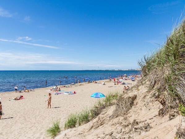 A beach with people sunbathing and swimming, a clear sky, and a distant view of wind turbines. - 4 Star Holiday Home in Falkenberg (Falkenberg)