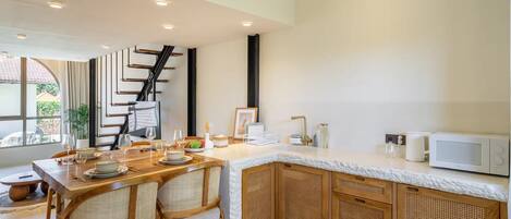 A modern kitchen with a dining area, featuring a wooden table set for four, a white countertop, and a staircase leading to another level.