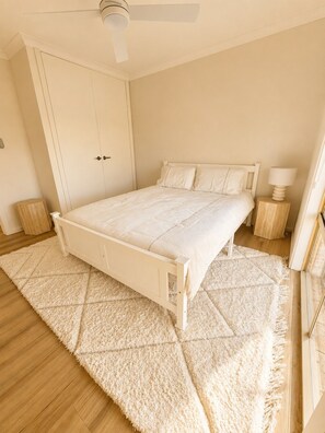 A bedroom with a bed, a bedside table, a nightstand, a ceiling fan, and a door.