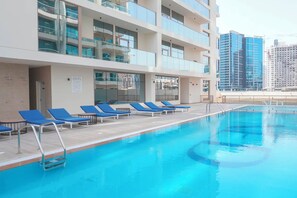 Ein Swimmingpool mit blauen Liegestühlen und ein mehrstöckiges Gebäude mit Glasfassade.