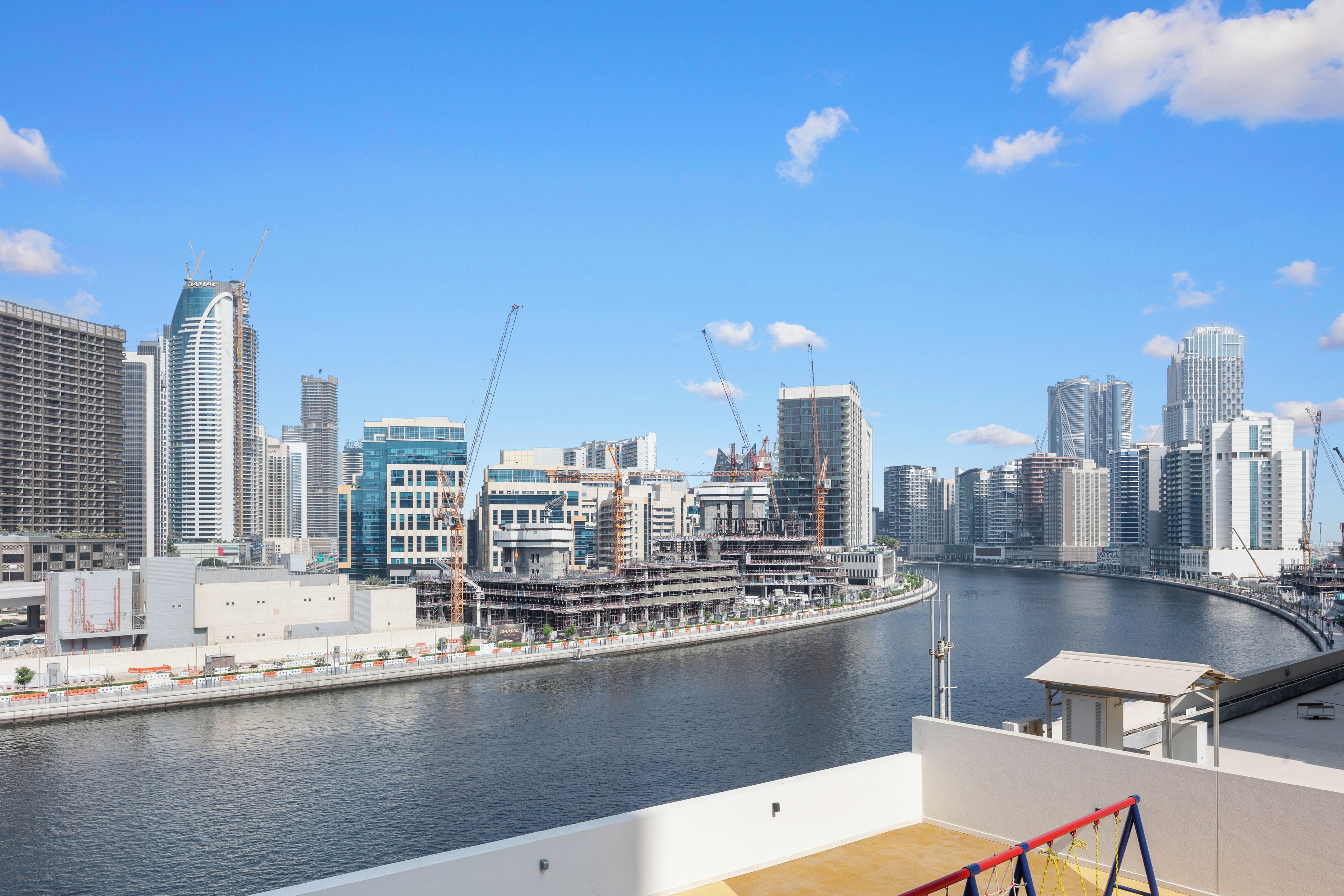Une vue urbaine comprenant une rivière, des immeubles de grande hauteur et des grues de construction.
