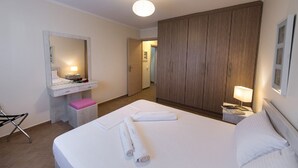 Hotellihuone, jossa on sänky, peilillä varustettu työpöytä, vaatekaappi, yöpöytä lampun kanssa ja tuoli.
