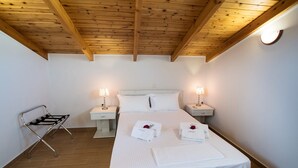 Ett hotellrum med ett träpanelat tak, en säng med vita sängkläder, två sänglampor, ett nattduksbord och en metallstol.