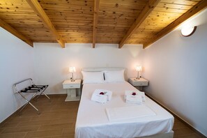 Ein Hotelzimmer mit Holzbalkendecke, einem Bett mit weißen Leinen, zwei Nachttischlampen, einem Nachttisch und einem Metallstuhl.